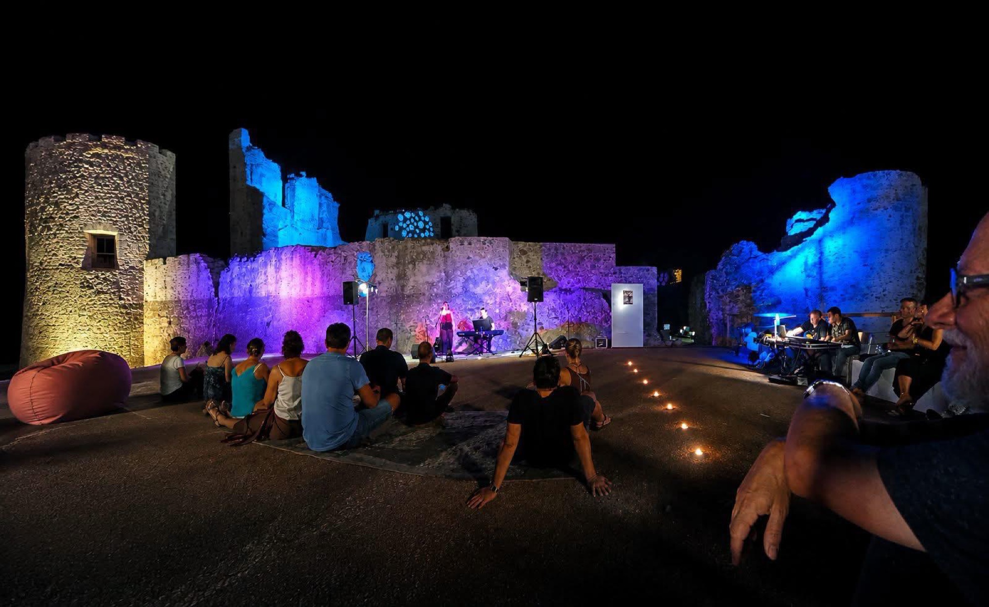 The audience on the ground before the stage, the castle walls lit against the night