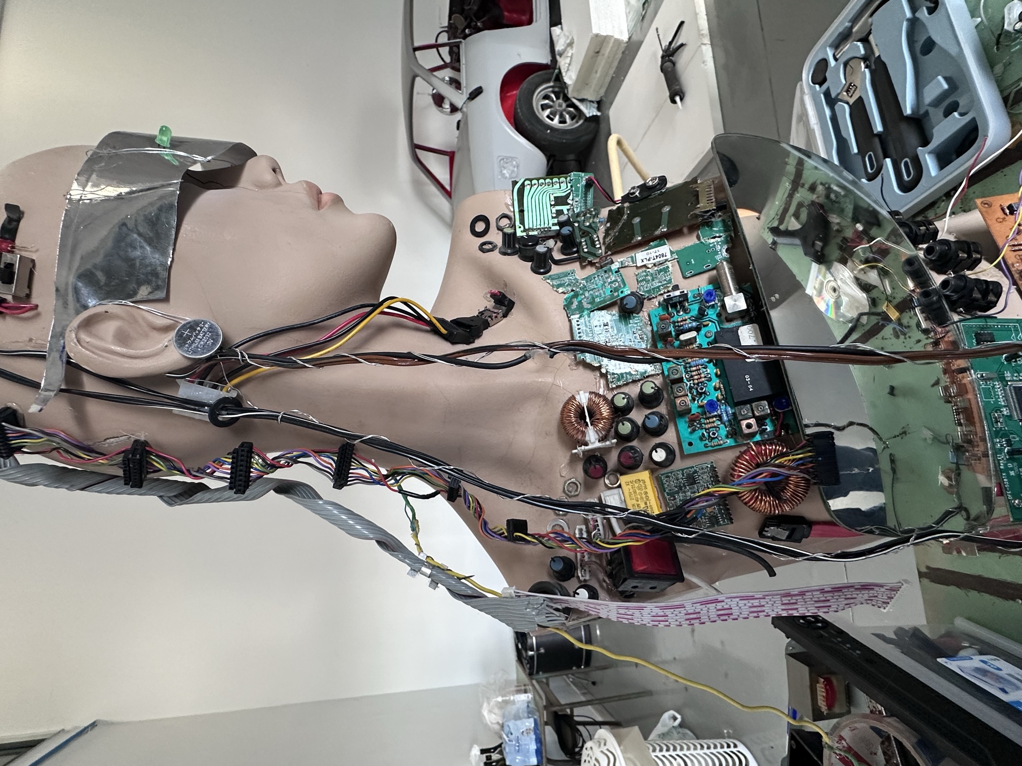 The cyborg mannequin up close with a car frame behind